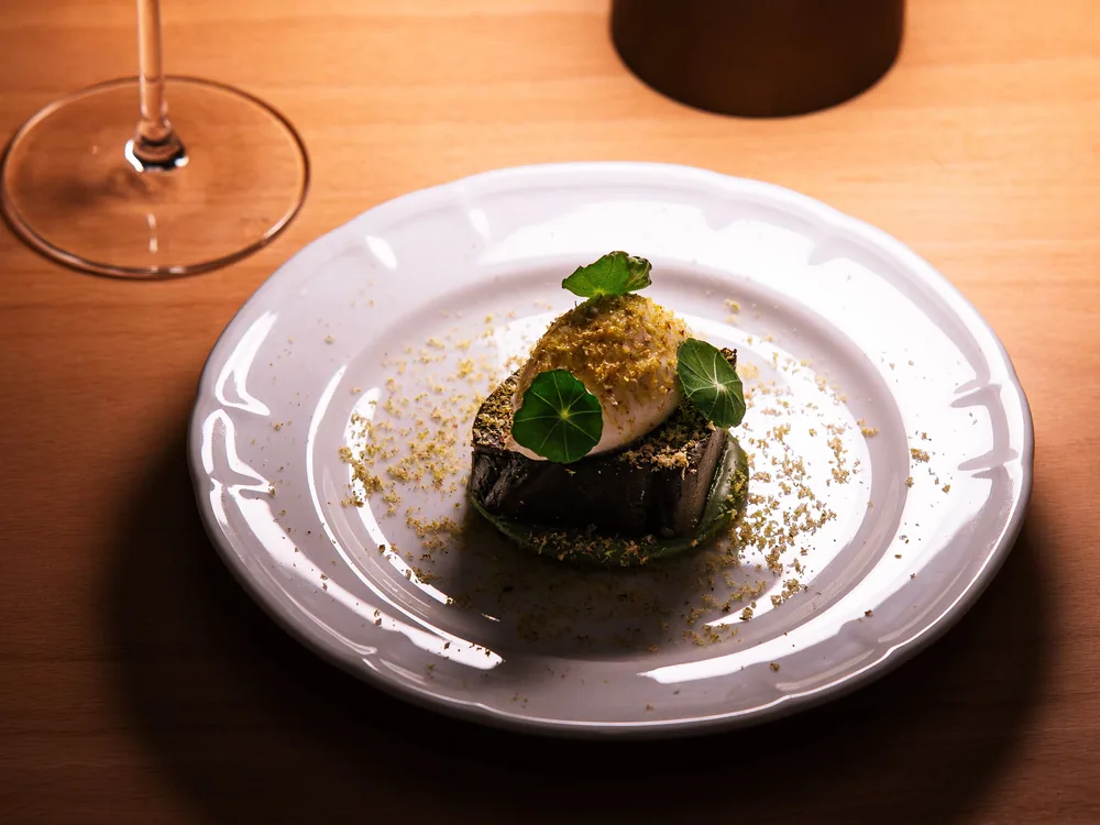 A single plated dessert with nasturtium leaves on a scalloped white plate, lit warmly on a wooden table